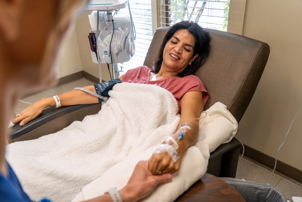 infusion center patient reclined on a chair receiving infusion and holding nurse hand