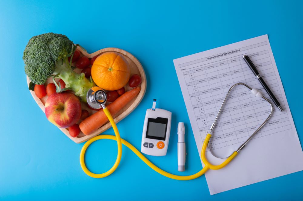 heart bowl filled with healthy fruit, glucometer and paper work next to it